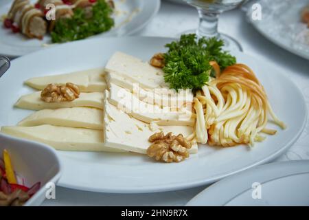 Different sorts of cheese. Cheese plate in the restaurant with different types of cheese, decorated with herbs and walnuts Stock Photo
