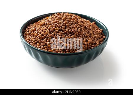 Raw wholegrain buckwheat groats in a blue bowl isolated on a white background. Roasted organic buckwheat grains for gluten free diet. Vegetarian food. Stock Photo