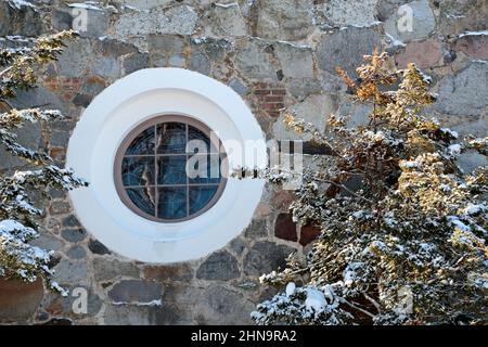A small round window with white frames on a stony church wall Stock Photo