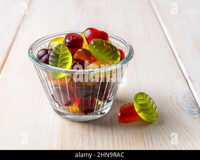 Colorful chewy candy in a glass bowl on a white wooden table. Multicolored gummy sweets made of fruit juice, sugar and gelatin. Jelly chews concept. Stock Photo