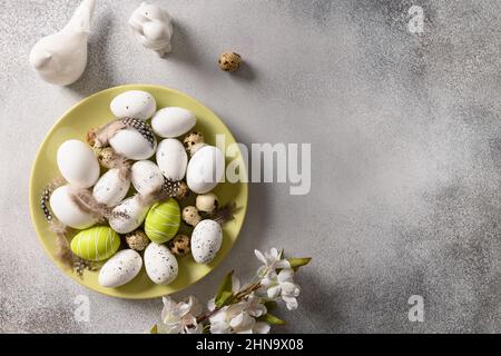 Easter eggs in green plate and spring decorations on gray background. View from above. Space for text. Concept egg dyeing, Stock Photo