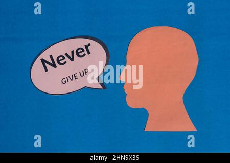 Paper human face with motivation text on speech bubble isolated on blue background. Conceptual image shows believing in yourself and willingness to ac Stock Photo