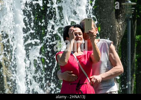 A couple aged 40+ are photographed near the fountain, taking selfies on a clear sunny spring day. Minsk (Belarus). May 9, 2018 Stock Photo