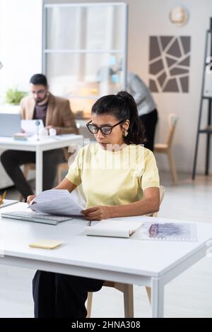 Serious businesswoman in eyeglasses doing paperwork at office, she sitting at her workplace and reading a contract Stock Photo