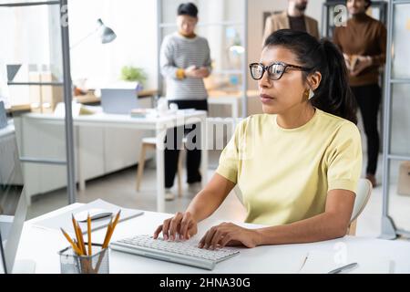 Serious businesswoman in eyeglasses concentrating on her work on computer, she sitting at the table and typing on computer keyboard Stock Photo