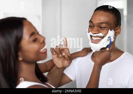 Loving Black Couple Having Fun In Bathroom, Laughing While Shaving Stock Photo