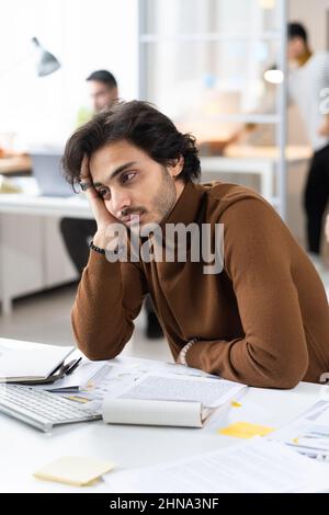 Young businessman sitting at his workplace at office with bored expression, he tired of paperwork Stock Photo