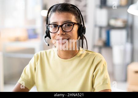 Portrait of call centre operator in headphones smiling at camera while working with clients at office Stock Photo