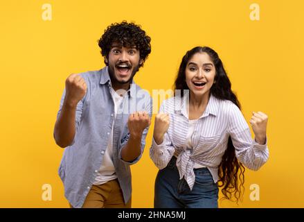 Portrait of overjoyed indian man and woman with open mouth cheering and staring at camera over yellow background Stock Photo