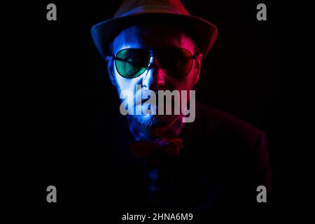 middle-aged man in a hat and aviator glasses in red and blue tones. photo in low-key Stock Photo