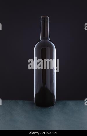 On a green wooden surface, in front of a black background, there is a bottle of red wine without a label. Stock Photo