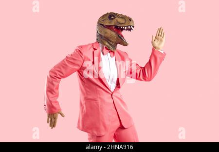 Funny man wearing pink suit and dinosaur mask dancing isolated on pink background Stock Photo