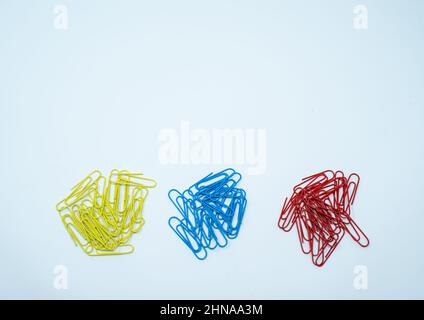 Multi coloured, blue, red and yellow paper clips in piles on a plain white background. Stock Photo