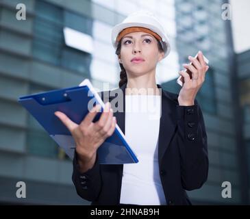 Woman architector in suit and hat is talking about project by the phone Stock Photo