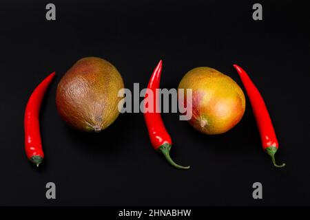 Whole mangoes and chili peppers on black background Stock Photo