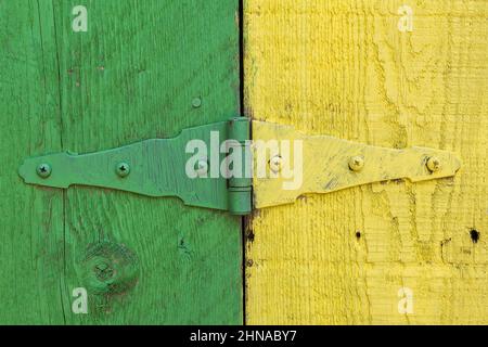 Close-up of green and yellow painted metal  door hinge plus grooves and saw marks on surface of  wood planks. Stock Photo