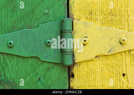 Close-up of green and yellow painted metal  door hinge plus grooves and saw marks on surface of  wood planks. Stock Photo