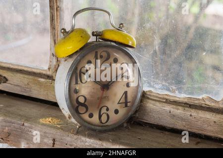 Antique Equity brand mechanical alarm clock on windowsill inside old rustic wood plank cabin. Stock Photo