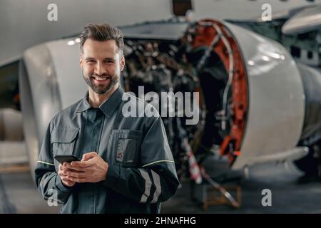 Cheerful airline mechanic using mobile phone in hangar Stock Photo
