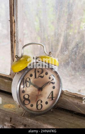 Antique Equity brand mechanical alarm clock on windowsill inside old rustic wood plank cabin. Stock Photo