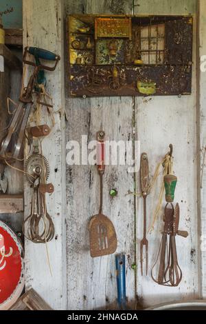 Antique hand tools and objects hanging on wall inside old rustic wood plank cabin. Stock Photo