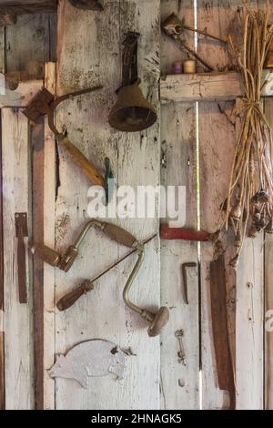 Antique hand tools and objects hanging on wall inside old rustic wood plank cabin. Stock Photo