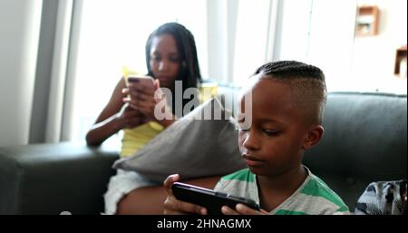 Casual African family relaxing at home sofa using technology. Black parents and kids each using their tech devices bubbles Stock Photo