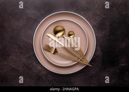 Collection of round beige plates on an old dark brown table, shabby board, top view. Golden cutlery and crockery for serving and eating. Modern craft Stock Photo