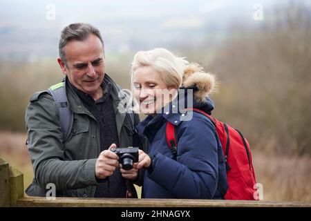 Mature Retired Couple Walk In Fall Or Winter Countryside Taking Photo On Digital Camera Stock Photo