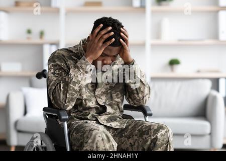 Upset black man sitting in wheelchair, wearing military uniform Stock Photo