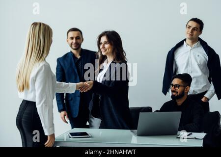 Smiling businesswomen shaking hands over conference table, company executive welcoming new business partner at diverse team meeting Stock Photo