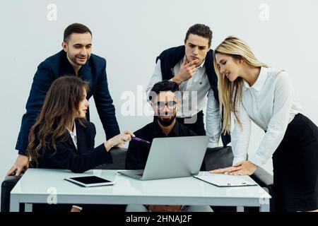 Smiling group of diverse businesspeople going over paperwork together and working on a laptop at a table in an office Stock Photo