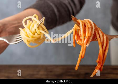 Two forks with white spaghetti on one side and spaghetti with tomato sauce on the other, connected together Stock Photo