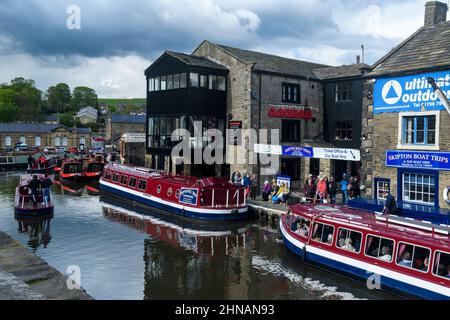 Busy popular tourist leisure experience on water (red boat moorings, men women sitting queuing) - scenic Leeds-Liverpool Canal, Yorkshire, England UK. Stock Photo