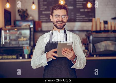 Joyful man barista using tablet computer in cafeteria Stock Photo