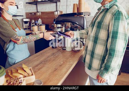Man using smartphone to pay for coffee in cafeteria Stock Photo
