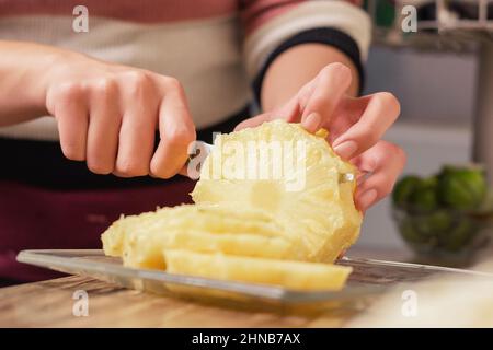 person slicing juicy yellow pineapple with a knife on wooden table in the comfort of their home Stock Photo