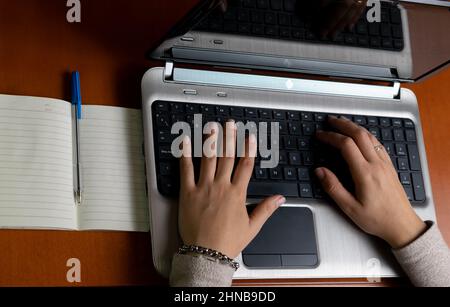 Top view of two hands of a person typing on the laptop with a notebook next to them Stock Photo