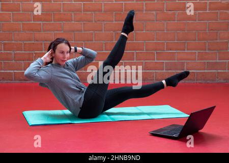 nice middle aged woman doing pilates lessons online on laptop Stock Photo