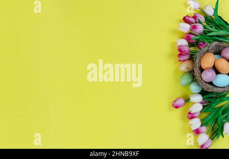 Right side border of tulip flowers, nest and colorful eggs on a bright yellow background for happy Easter holiday season concept Stock Photo