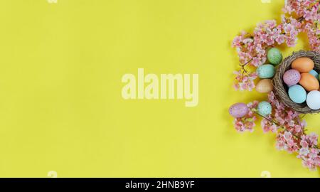 Right side border of cherry blossom flowers, nest and colorful eggs on a bright yellow background for happy Easter holiday season concept Stock Photo