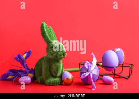 Cute Easter bunny with painted eggs and flower on red background Stock Photo