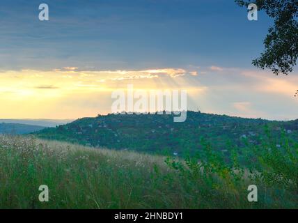 The grass is on the slope, the rays of the sun are breaking through from behind the clouds. Siberia, Russia Stock Photo