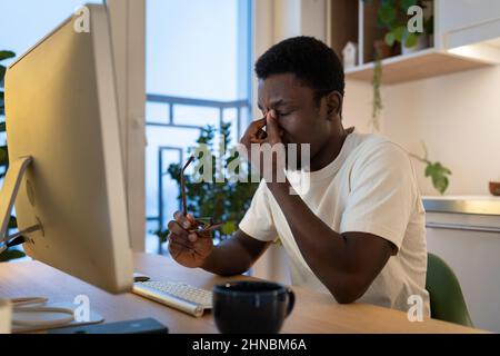 Tired guy remote web developer take off glasses feel eye strain after overtime computer work at home Stock Photo