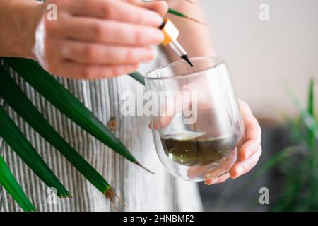 Woman hand holding dropper with green chlorophyll at home. Immunity booster concept  Stock Photo