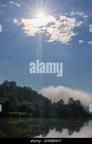 sun rays breaking through clouds floating above surface of water Stock Photo