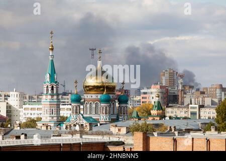 View of Russian city with roofs of buildings and beautiful orthodox church. black smoke from fire in background Stock Photo