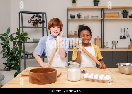 Boys wrapped up in reading recipe with help of digital tablet while standing at wooden kitchen table in order to make surprise for Mothers Day, portrait shot Stock Photo