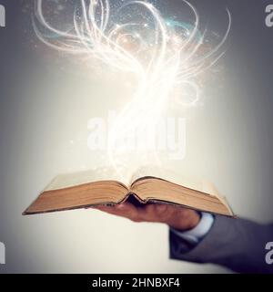 Literacy is a gift that keeps on giving. Shot of a hand holding an open storybook with light emanating from it. Stock Photo