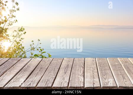 An empty wooden deck or table against the backdrop of a calm morning lake at dawn in pastel colors. Product display frame. Stock Photo